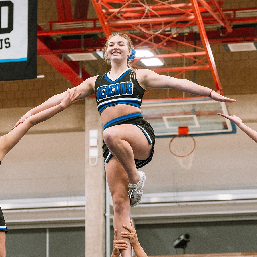 A UMass Boston cheerleader being lifted in a balance by her team.