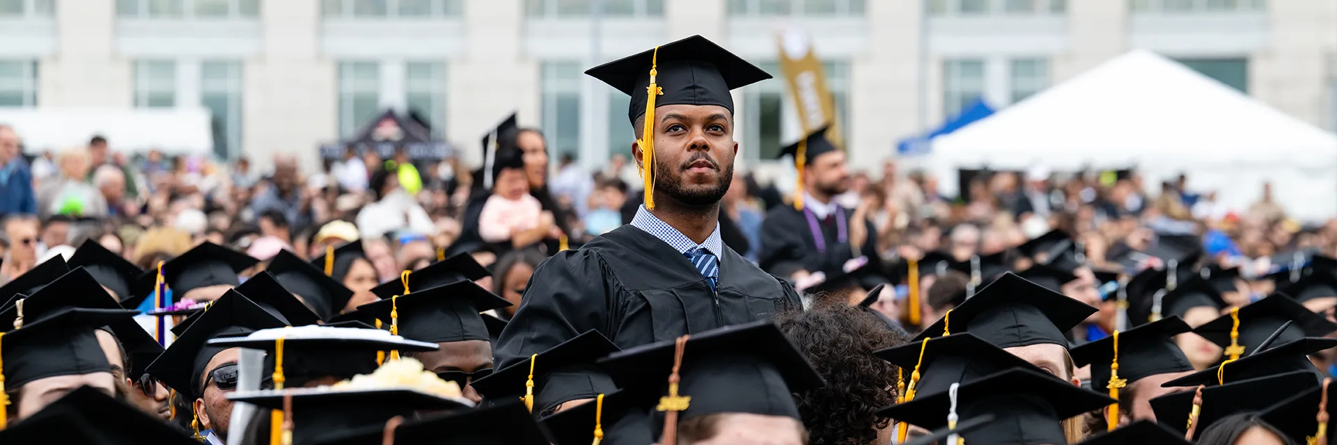 <figure><img src="/media/umassboston/editor-uploads/rooted-amp-rising/student-access-success_kprince_-11-1920x640.webp" alt="Student in cap in gown stands up in crowd at Commencement in front of the Campus Center." style="width : -1px; height : -1px;     " /></figure>