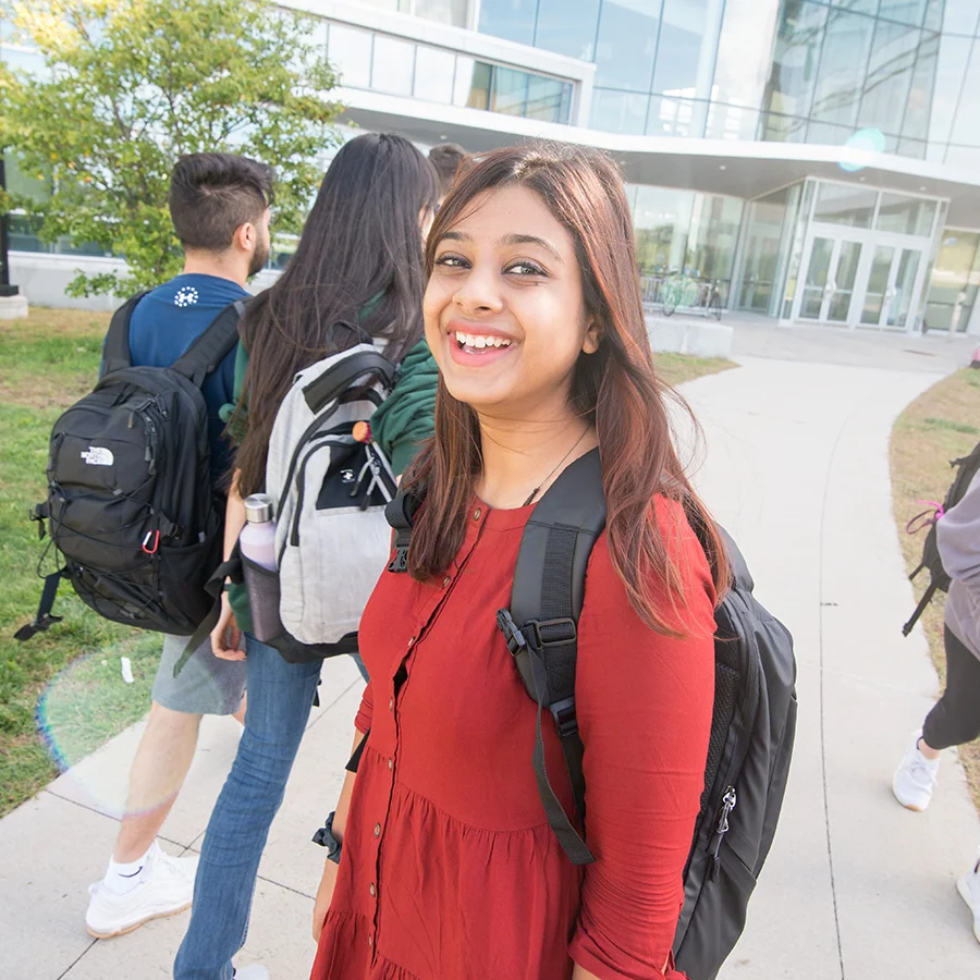 A smiling student with backpack in front of the Integrated Sciences Complex.